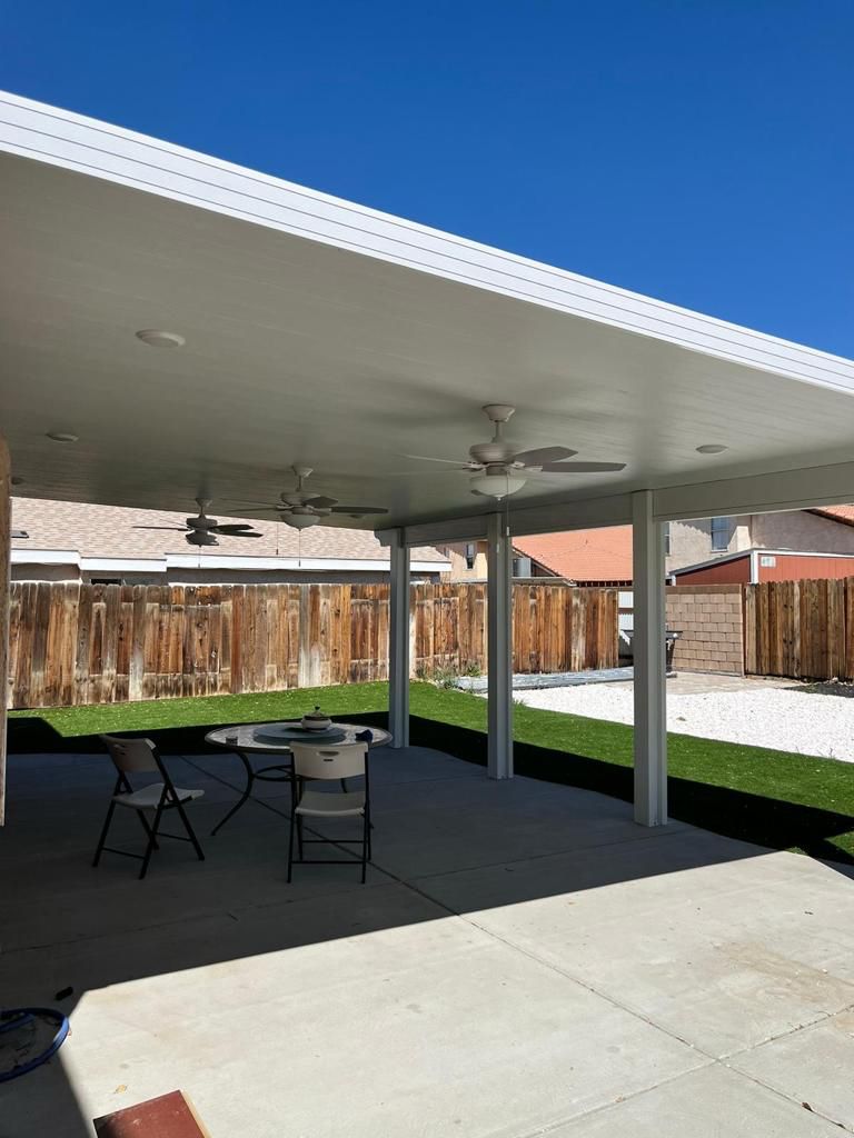 Covered patio with ceiling fans and a table on concrete floor.